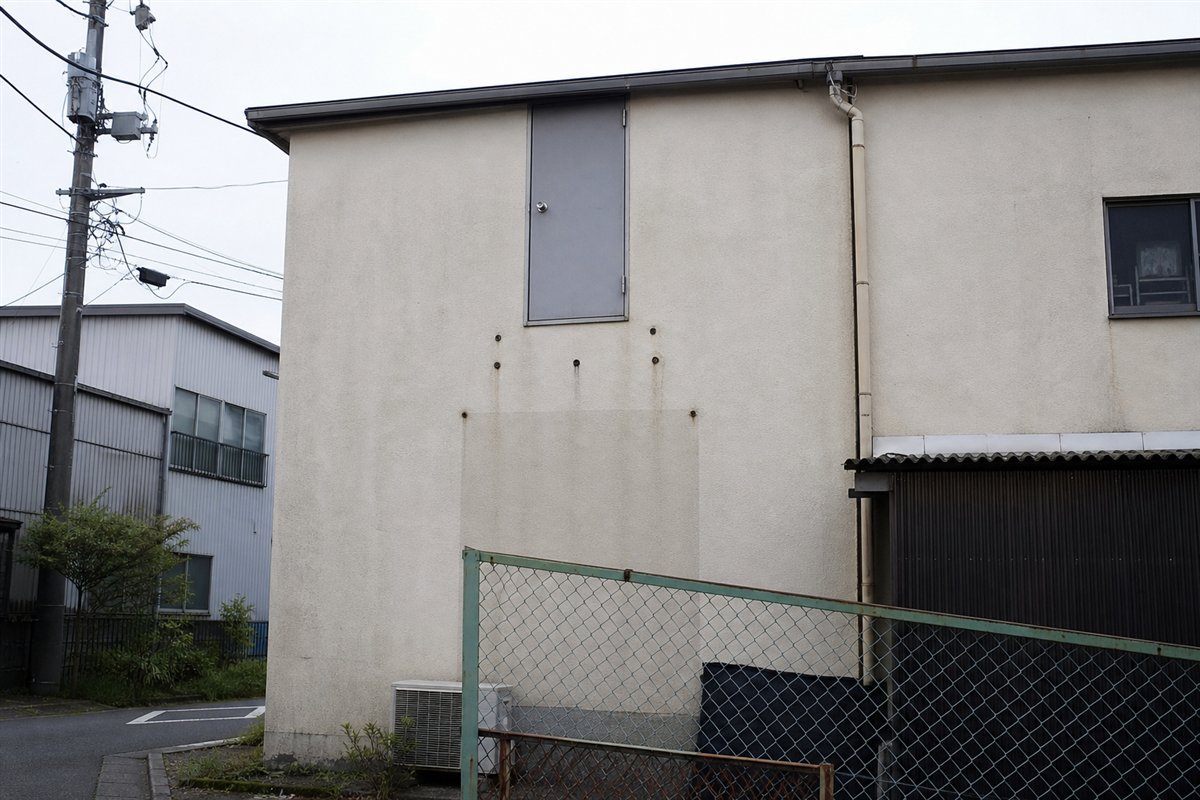 二階の金属扉だけが外壁に残り、かつての階段と踊り場は完全に撤去され、ボルト跡だけが見える
