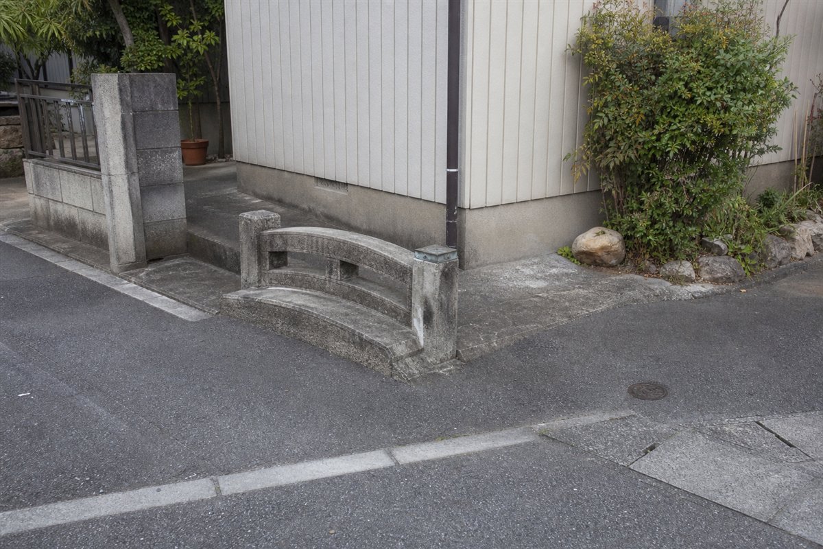 側溝が舗装で完全に埋められた後も、短いコンクリート橋と低い欄干だけが道路沿いに残る