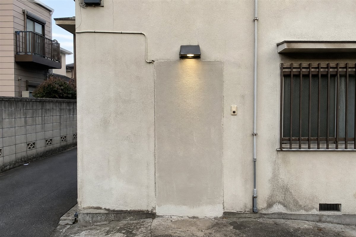 撤去され壁で塞がれた玄関の上に、古い玄関灯だけが配線されたまま残っている