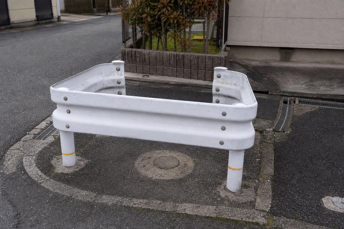撤去された電柱か樹木の跡を囲むように、短い白いガードレールが空のアスファルトだけを守っている