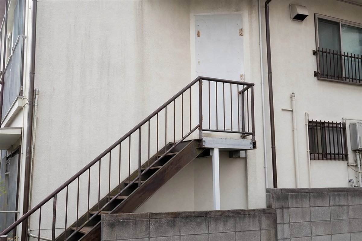 外階段の小さな踊り場が、扉を塞いだ跡の残る壁面に接続し、手すりまできれいに維持されている