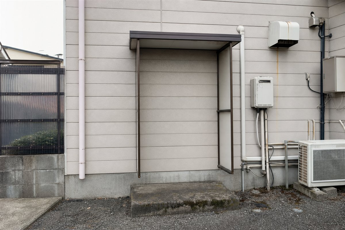 勝手口は同色の外壁材で塞がれたのに、庇と両脇の風除けパネルだけが入口の形を保っている