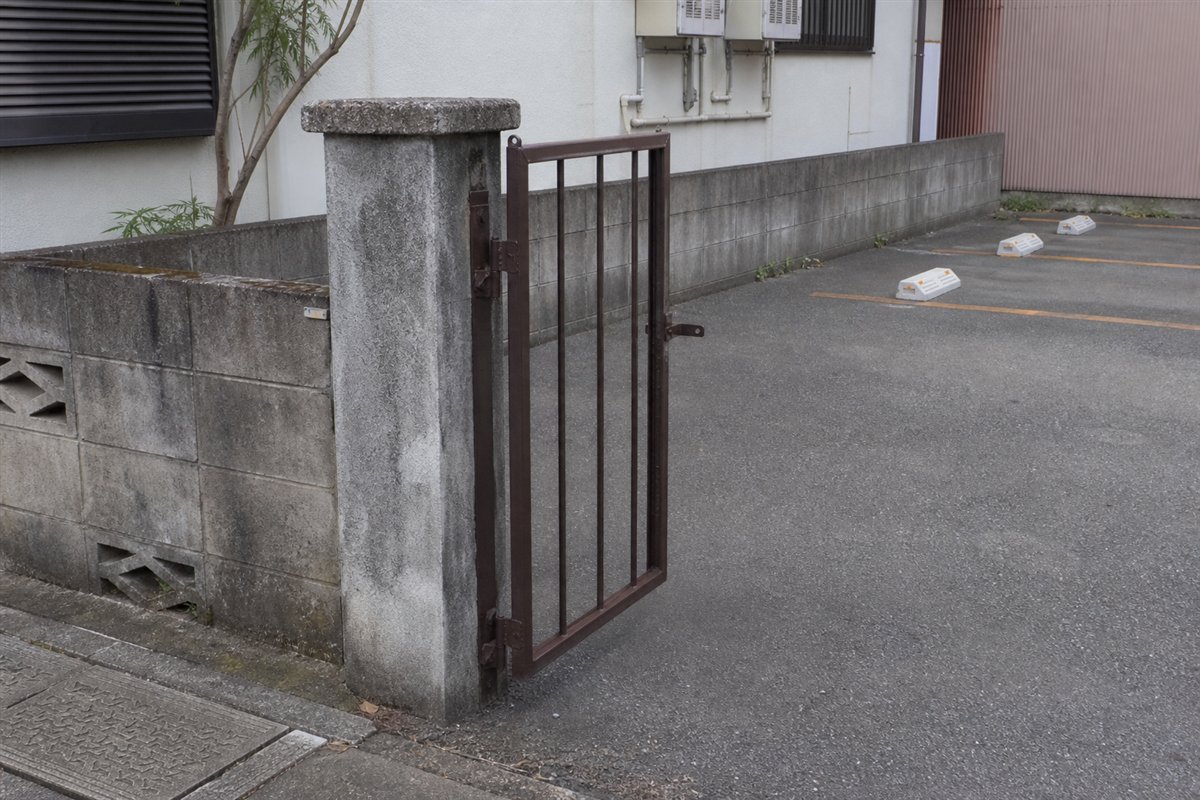 片側の塀と門柱は撤去されたのに、片開き門扉の一枚だけが残った門柱へ蝶番で固定されている