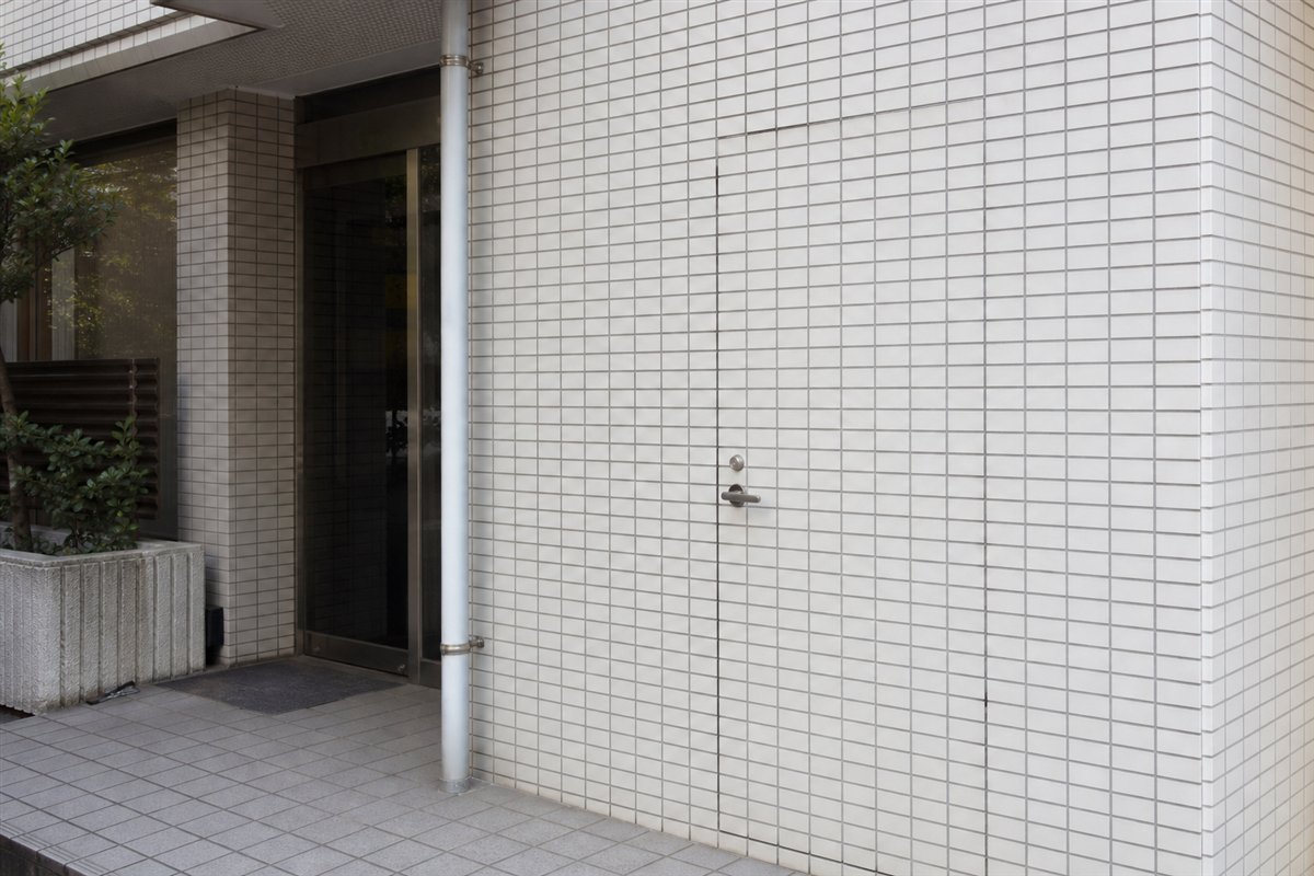 扉は周囲と同じタイルで完全に塞がれているが、鍵穴付きの古いレバーハンドルだけが元の位置に残る