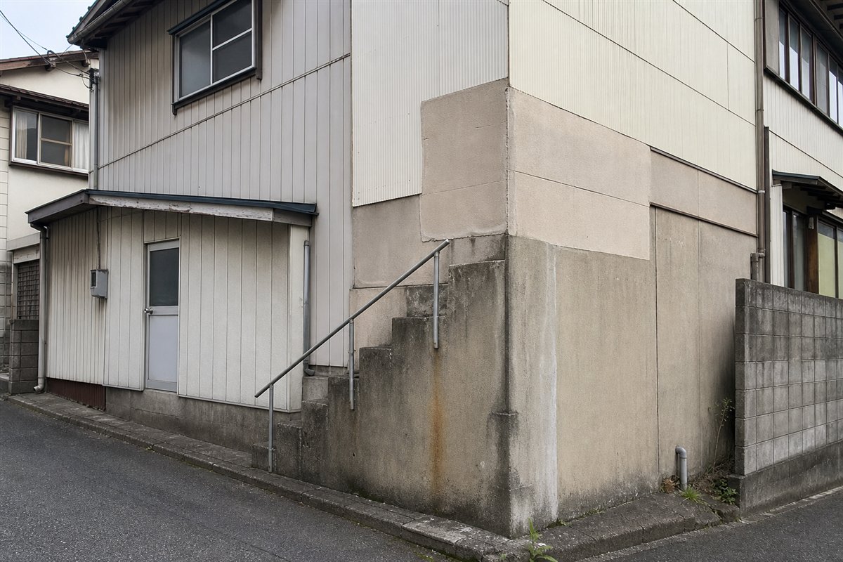 屋外コンクリート階段の上半分が後から増築された外壁に埋まり、下半分だけが地面から壁へ続いている