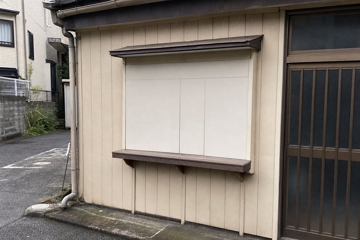 受け渡し窓は板と塗装で塞がれているが、低いカウンター棚と雨よけだけが外壁に残る