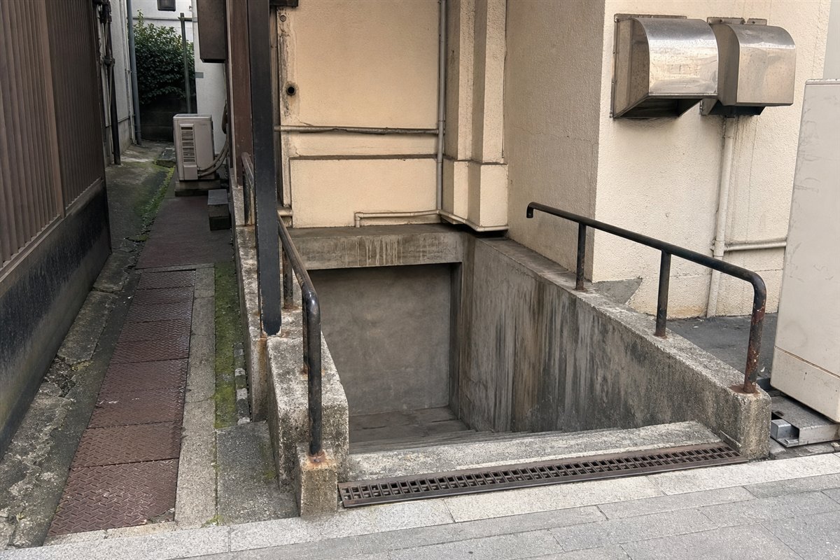 地面から数段下るコンクリート階段があるが、地下入口は厚いコンクリート壁で塞がれ、排水口だけが残る