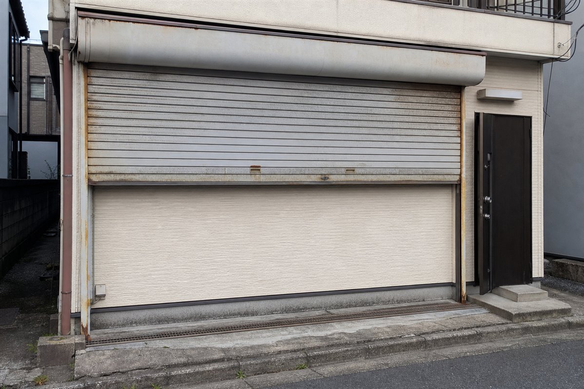 古い金属シャッターを少し上げると、そのすぐ後ろが新しい住宅外壁で完全に塞がれているのが見える