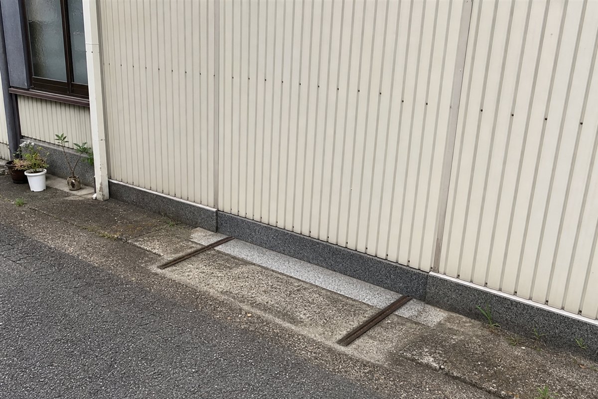 通用門は波板外壁で塞がれているが、御影石の敷居と戸車レールだけが地面に残っている